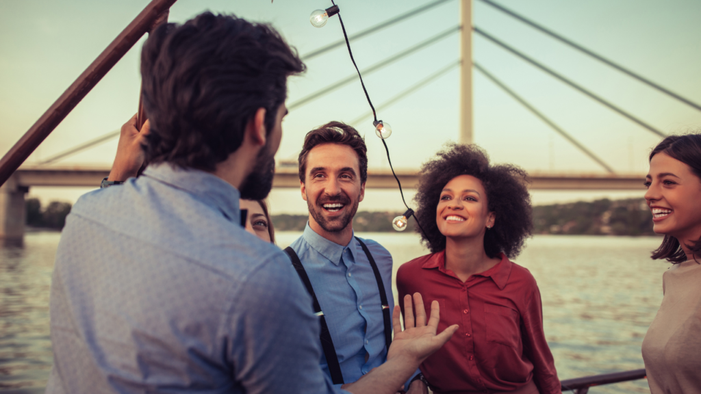 A man in a blue button up tells a story to a group of people overlooking a lake.